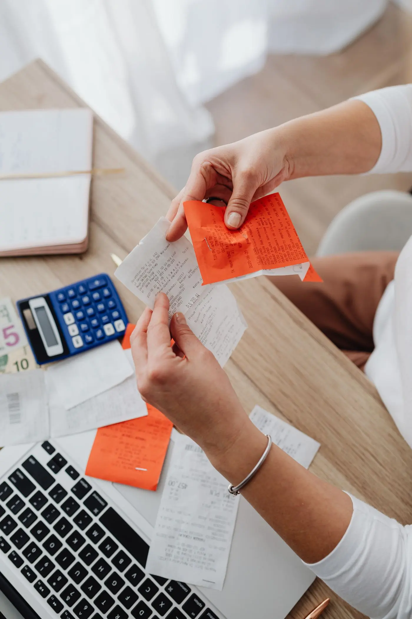 Two people passing paper receipts across a desk beside a calculator and a keyboard