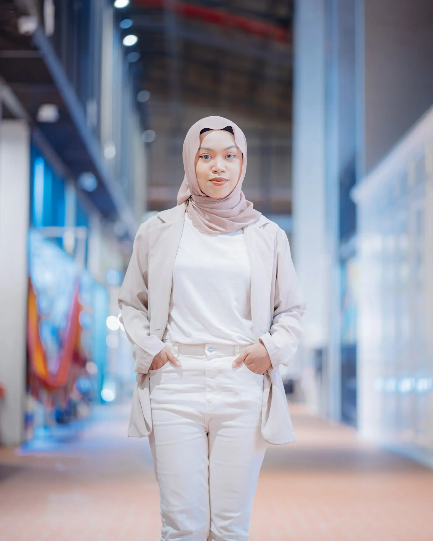 A smiling woman in a hijab and blazer standing in a bright modern office corridor